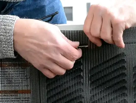 صورة مقربة لفلتر مكيف بين يدي شخص، مع ظهور الجزء الخلفي من المكيف بشكل غير واضح في الخلفية، مما يبرز حجم الفلتر مقارنة بالوحدة.