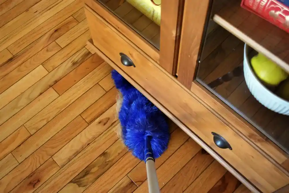 ممسحة طويلة تصل إلى الزوايا وتحت الأثاث لإزالة الغبار المتراكم، توضح أماكن غالبًا ما يغفل عنها تنظيف الشركات الرخيصة.