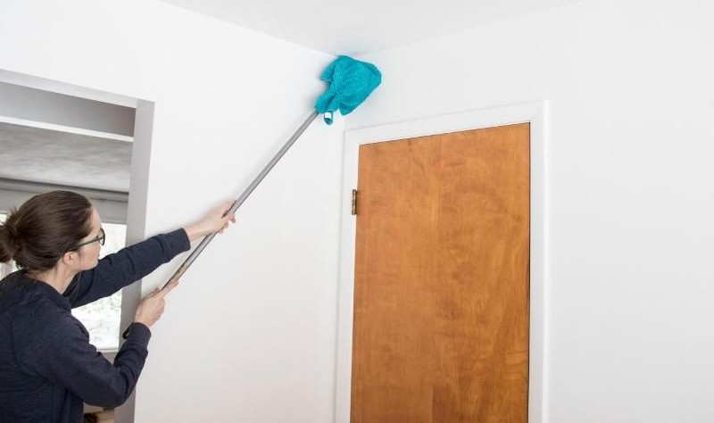 امرأة تستخدم ممسحة طويلة لتنظيف الزوايا المرتفعة والغبار فوق الأبواب في المنزل