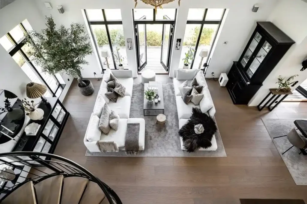 "غرفة معيشة كبيرة داخل فيلا حديثة، تحتوي على أرائك بيضاء وأرضية خشبية واسعة، مع أسقف مرتفعة وممرات متعددة، مناسبة لتوضيح الجهد الزمني والمواد المستخدمة في التنظيف"