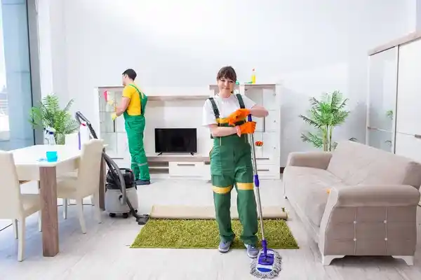 منظفون يعملون داخل غرفة معيشة حديثة بينما المالك يراقب منهمكًا، يظهر تقييم جودة النظافة في المنزل.