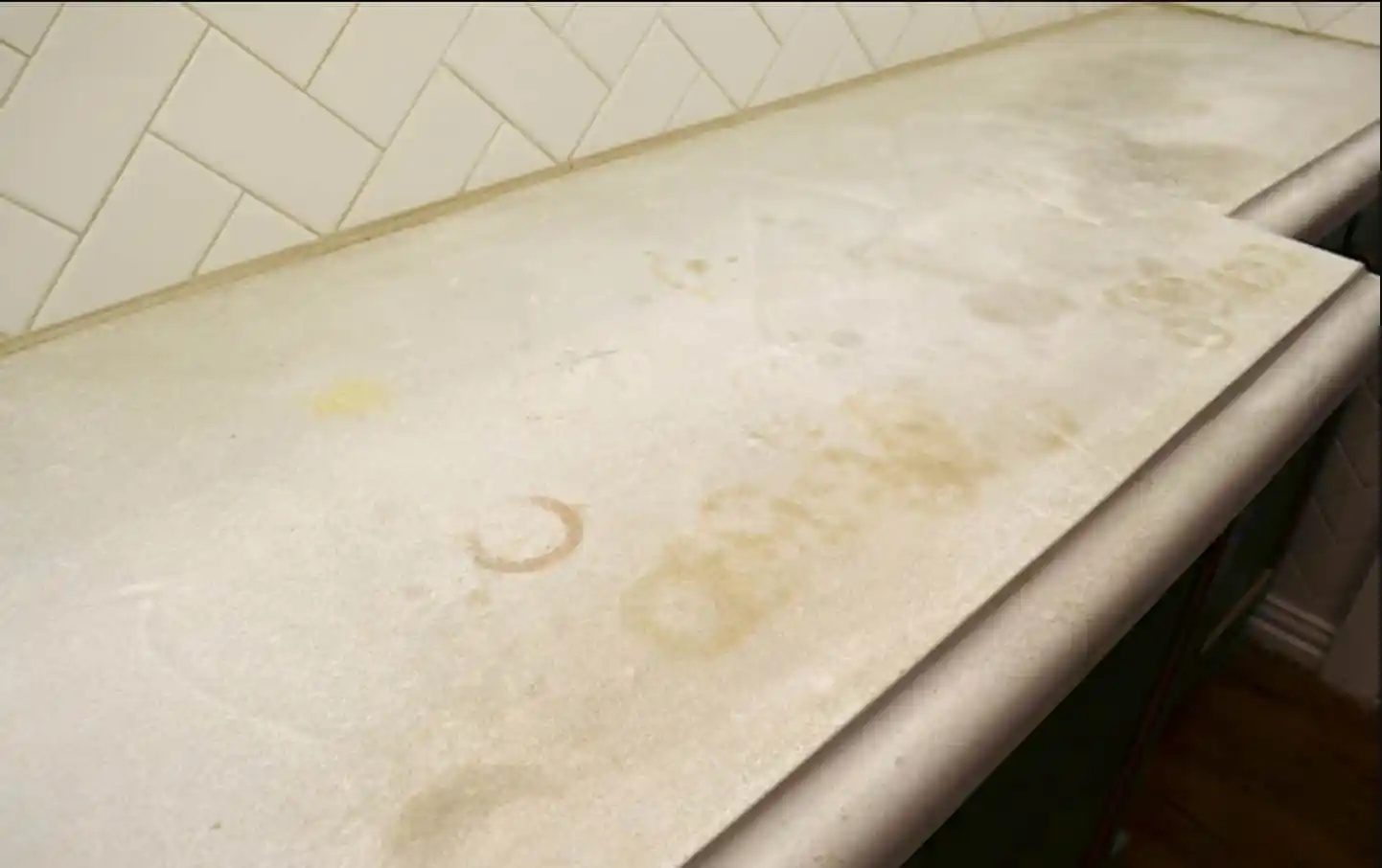 سطح كونتر في المطبخ عليه بقع ودوائر لطلاء متضرر، يوضح تأثير التنظيف القاسي أو استخدام مواد خاطئة على أسطح العمل.