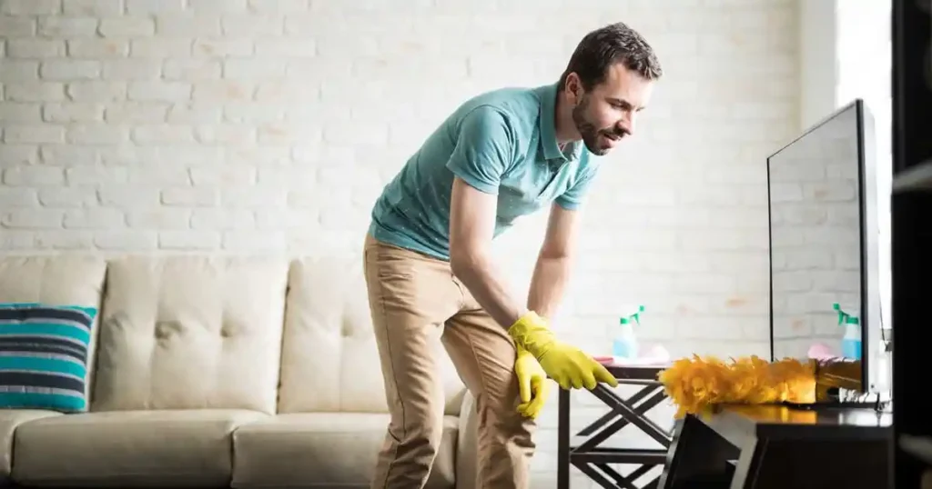 شخص ينظف ويزيل الغبار من أسطح غرفة الجلوس، في مشهد يوضح أهمية الاهتمام بالتفاصيل بعد عملية التنظيف.