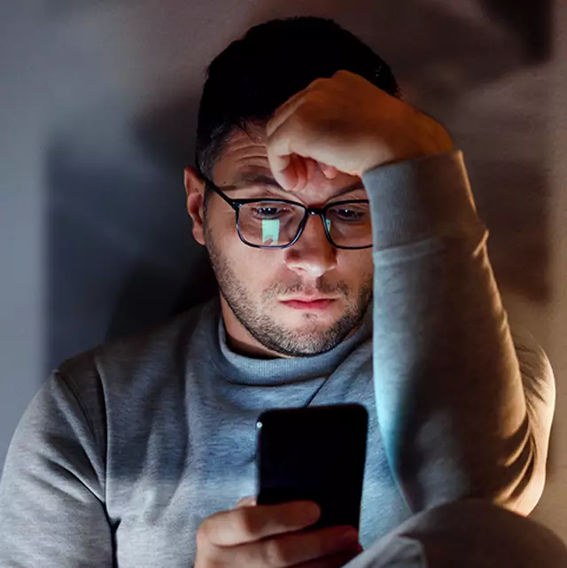 رجل سعودي يشعر بالقلق ويبحث عن تطبيق صيانة مكيفات عبر هاتفه في غرفة مظلمة