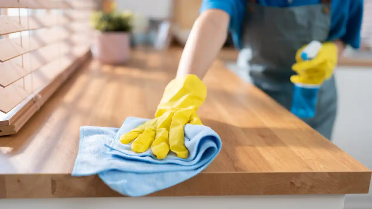 عامل تنظيف محترف يستخدم قطعة قماش ميكروفايبر لتنظيف الأسطح الخشبية بدقة